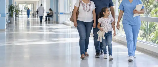 Familia caminando por un pasillo luminoso de hospital público junto a una enfermera, con un lapacho en flor afuera